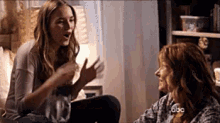 two women are sitting next to each other on a couch talking to each other .