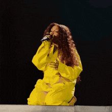 a woman singing into a microphone wearing a yellow jumpsuit