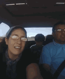 a woman wearing glasses smiles while sitting in a car with two other people
