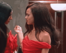 a woman in a red off the shoulder dress looks at another woman