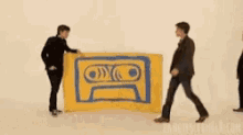 a group of men are standing around a large yellow flag with a cassette tape on it