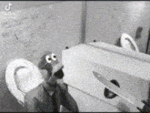 a black and white photo of a puppet holding a knife next to a toilet .