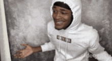 a man wearing a white hoodie is standing in front of a wall and smiling .