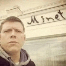 a man is taking a selfie in front of a building with a sign that says minet .