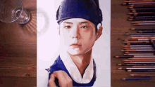 a drawing of a man wearing a blue hat is on a table next to colored pencils