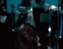 a man is covering his face with his hands while holding a microphone in a dark room .