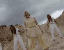 a group of women are standing in a desert wearing white pants