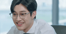 a man wearing glasses and a white shirt smiles for the camera