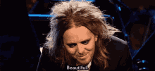 a man with long hair is smiling and saying beautiful in front of a microphone