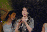 a woman in a striped shirt is singing into a microphone while standing next to two other women in a dark room .