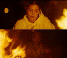 a woman in a white hoodie sits next to a man in a plaid shirt in front of a fire