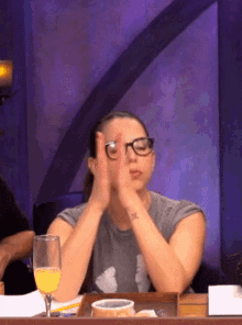 a woman wearing glasses is sitting at a table with a glass of wine
