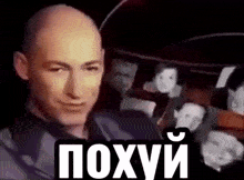 a bald man is smiling in front of a group of people with russian writing on it .