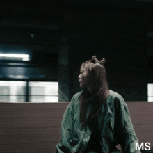 a woman wearing a green jacket with the letters ms on the bottom right