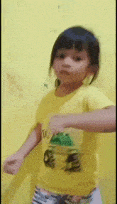 a little girl in a yellow shirt is dancing in front of a yellow wall .