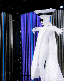 a person in a white costume with a bowl on their head and a purple curtain behind them