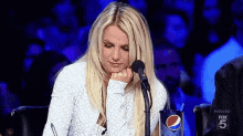 britney spears is sitting in front of a microphone while holding her hand to her chin .
