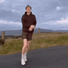 a man in shorts and a hoodie is running down a road .