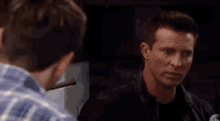 two men are standing next to each other in a dark room and talking to each other .