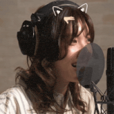 a woman wearing headphones and a cat ear headband sings into a microphone