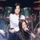a girl singing into a microphone while another girl plays drums