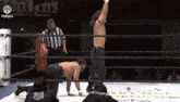 two men are wrestling in a ring with a referee standing behind them .