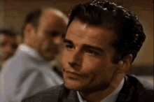 a close up of a man 's face in a suit and tie with a man in the background .