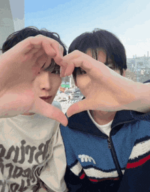 two young men are making a heart shape with their hands and one has a shirt that says mira