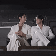two men in white suits are sitting next to each other in a dark auditorium