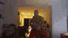 a shirtless man in red shorts is dancing in a dark room