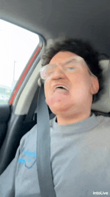 a man wearing glasses is sitting in a car with a seat belt around his neck