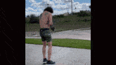 a shirtless man with tattoos on his back is standing on a sidewalk .