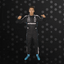 a man in a petronas racing suit is standing with his arms outstretched