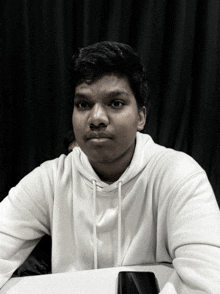 a young man wearing a white hoodie looks at the camera