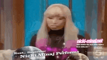 a woman with blonde hair is sitting in front of a screen that says next superstar nicki minaj performs .