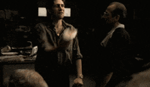 two men are standing next to each other in a dark room and talking .