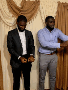 a man in a suit and a man in a blue shirt are standing in front of a curtain