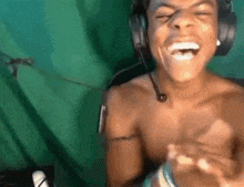 a shirtless man wearing headphones and a microphone is laughing in front of a green screen .