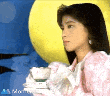a woman in a pink dress is holding a cup of tea in front of a yellow moon and the word momento is on the bottom right