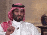 a man wearing a keffiyeh and a white shirt is sitting in a chair and pointing .