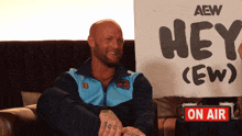 a man sitting on a couch holding a sign that says hey crew