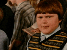 a young boy wearing a striped vest looks at the camera with a serious look on his face