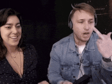 a man wearing headphones and a denim jacket talks to a woman