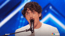 a man singing into a microphone with nbc written on the bottom