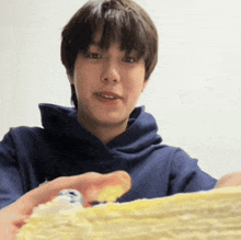 a man in a blue hoodie is holding a piece of cake in his hand