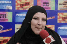 a woman wearing a hijab is talking into a microphone in front of a wall that says power