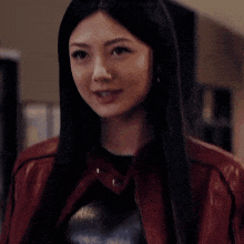 a woman with long black hair and a red jacket is looking at the camera .