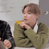 a man in a green sweater is sitting at a table holding a piece of cheese .