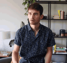 a man in a polka dot shirt stands in front of a bookshelf with books on it