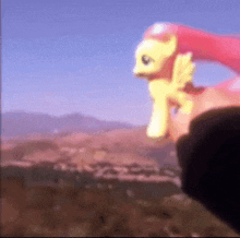 a person is holding a pink and yellow toy pony with wings